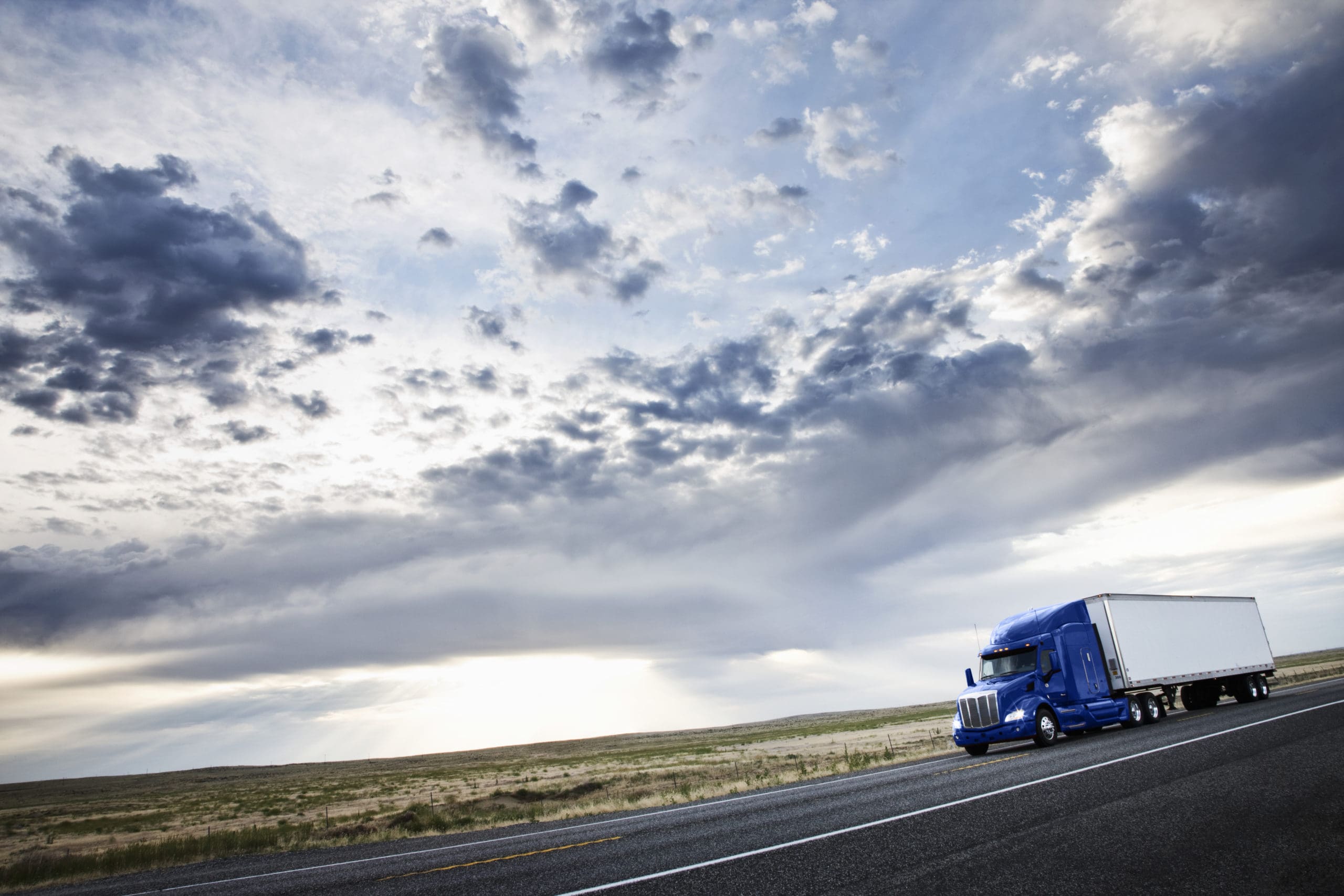 a blue semi truck driving with a view of the sky behind it